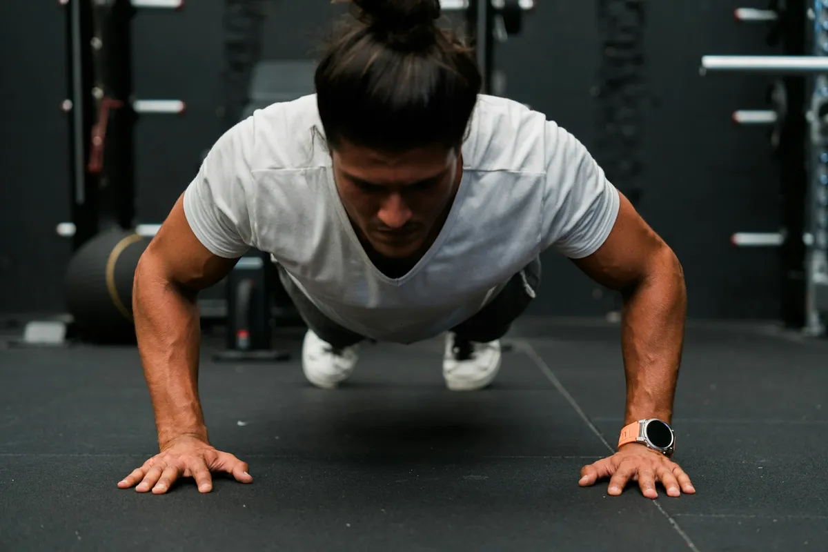 A man at the bottom of a push-up on a gym floor, hands under his shoulders